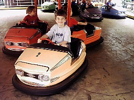 Boy sitting in a bumper car, while being told by park ride attendant to avoid head-on collisions.